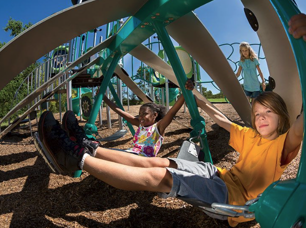 Kids playing on modern park playground equipment with climbing features and swings, part of a city playground installation.