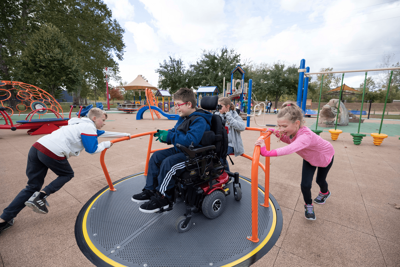 Kids playing on an inclusive spinner at a park playground