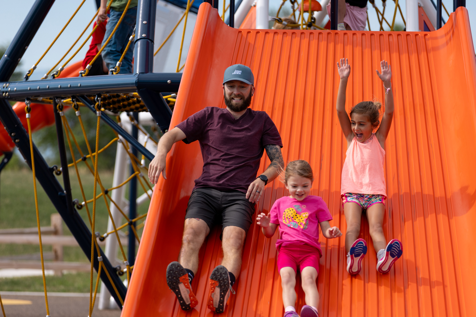 Multi-generational, cross-generational family sliding down a big slide at a playground