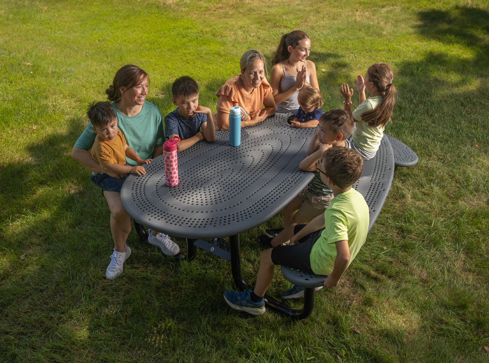 Two adults and children, of multiple ages, sitting at a Community Table.